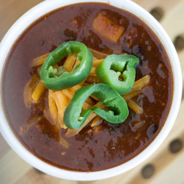 Close-up of a bowl of chili topped with shredded cheddar cheese and sliced jalapeños.