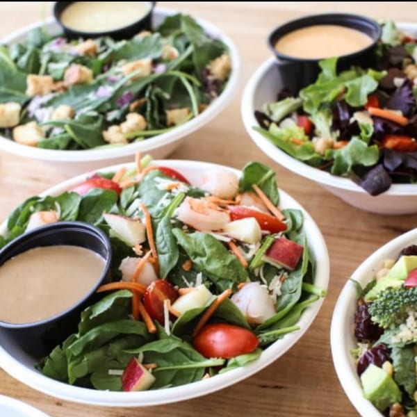 Four vibrant Bliss & Vinegar salads with various fresh ingredients and dressings in white bowls.