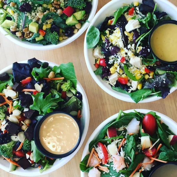 Four vibrant Bliss & Vinegar salads in white bowls, featuring fresh greens, diverse toppings, and dressings.